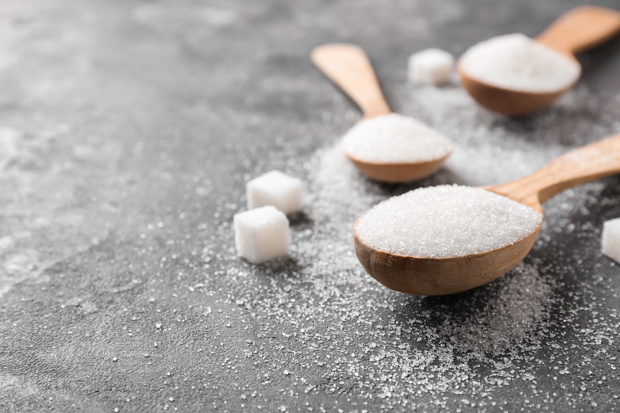 Spoons with pure sugar on grey background